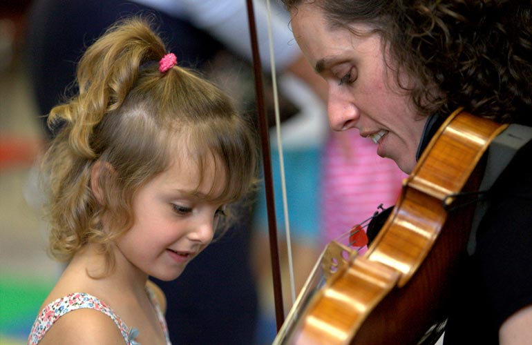 Violist Caitlin Boyle leans in and shows a young girl her viola.