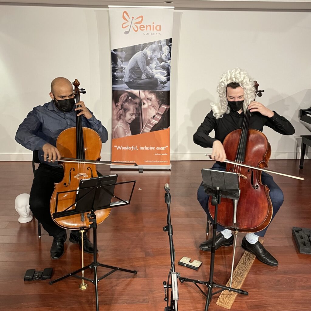 VC2 Cello Duo performing at TO Live. Amahl (left) is playing the cello and Bryan (right) is also playing while wearing a wig.