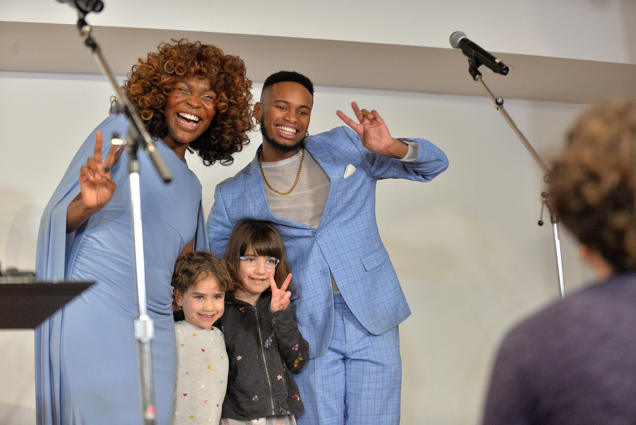 Two performers and two children pose on a concert stage for a photo